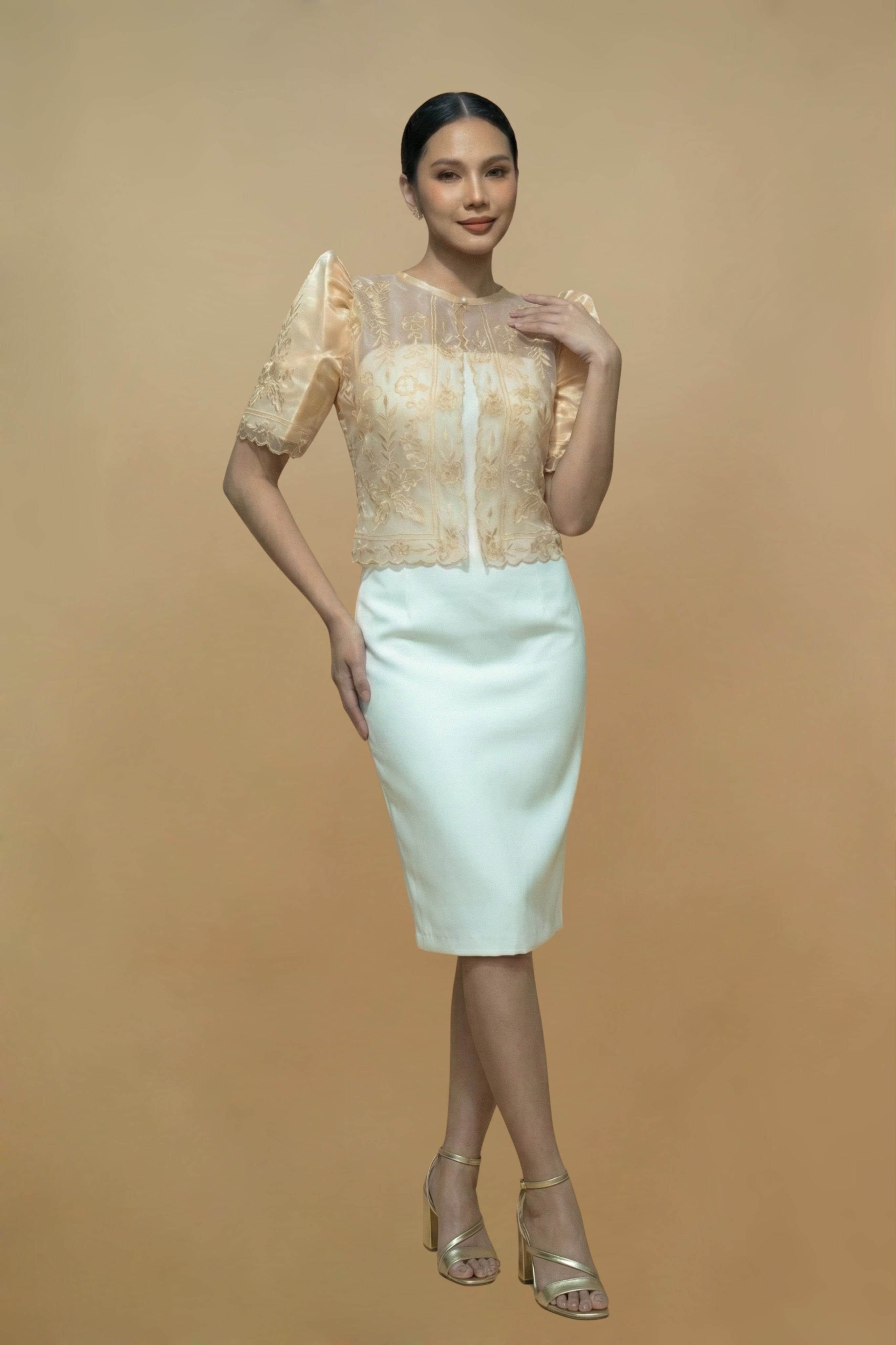 Woman wearing a beige Filipiniana Bolero top and white pencil skirt on a beige background