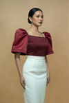 Woman wearing a burgundy Filipiniana Kimona top with puff sleeves and a white skirt on a beige background
