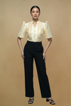 Woman wearing a cream blouse with ruffled sleeves and black pants on a beige background