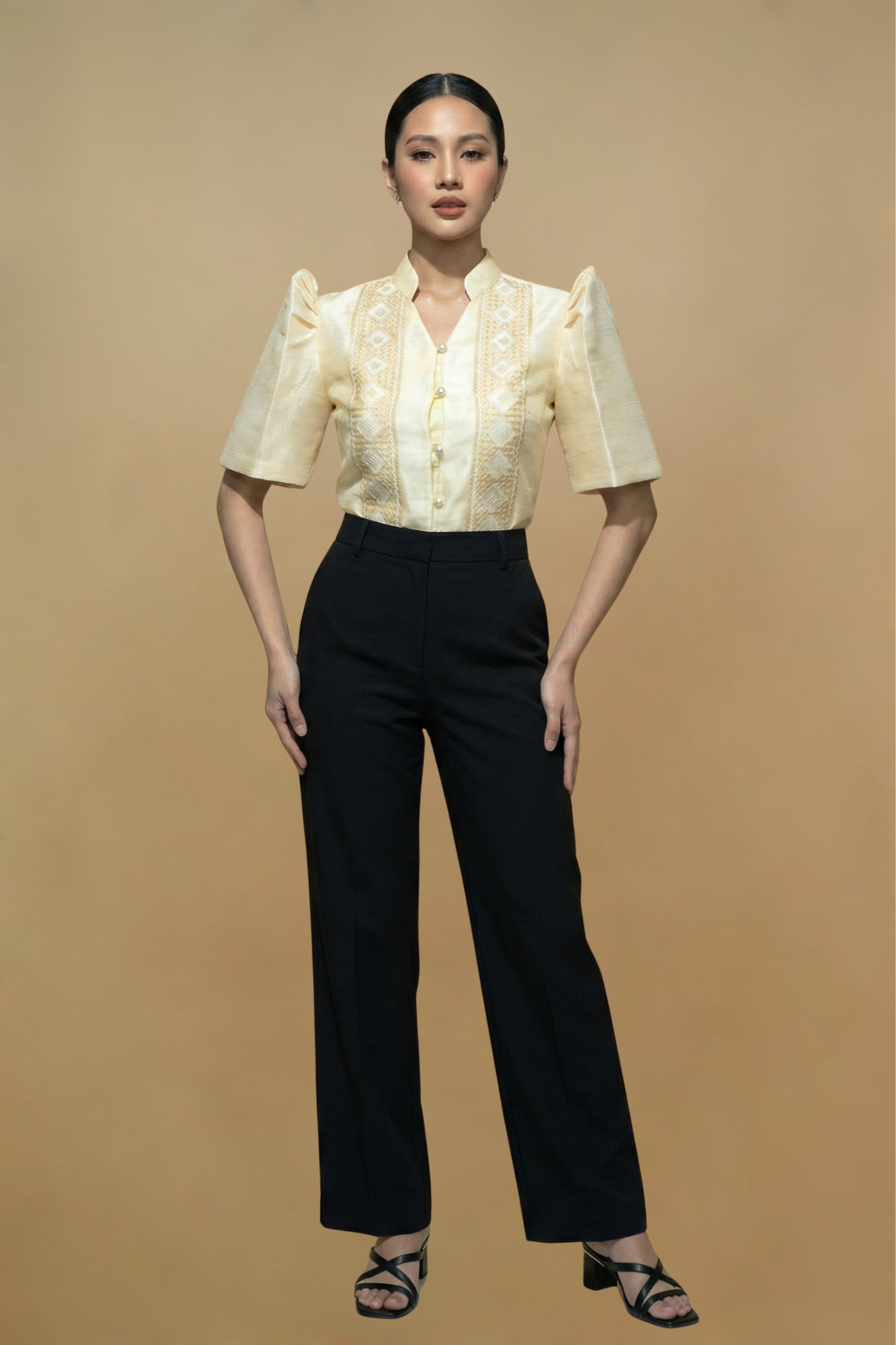 Woman wearing a cream blouse with ruffled sleeves and black pants on a beige background
