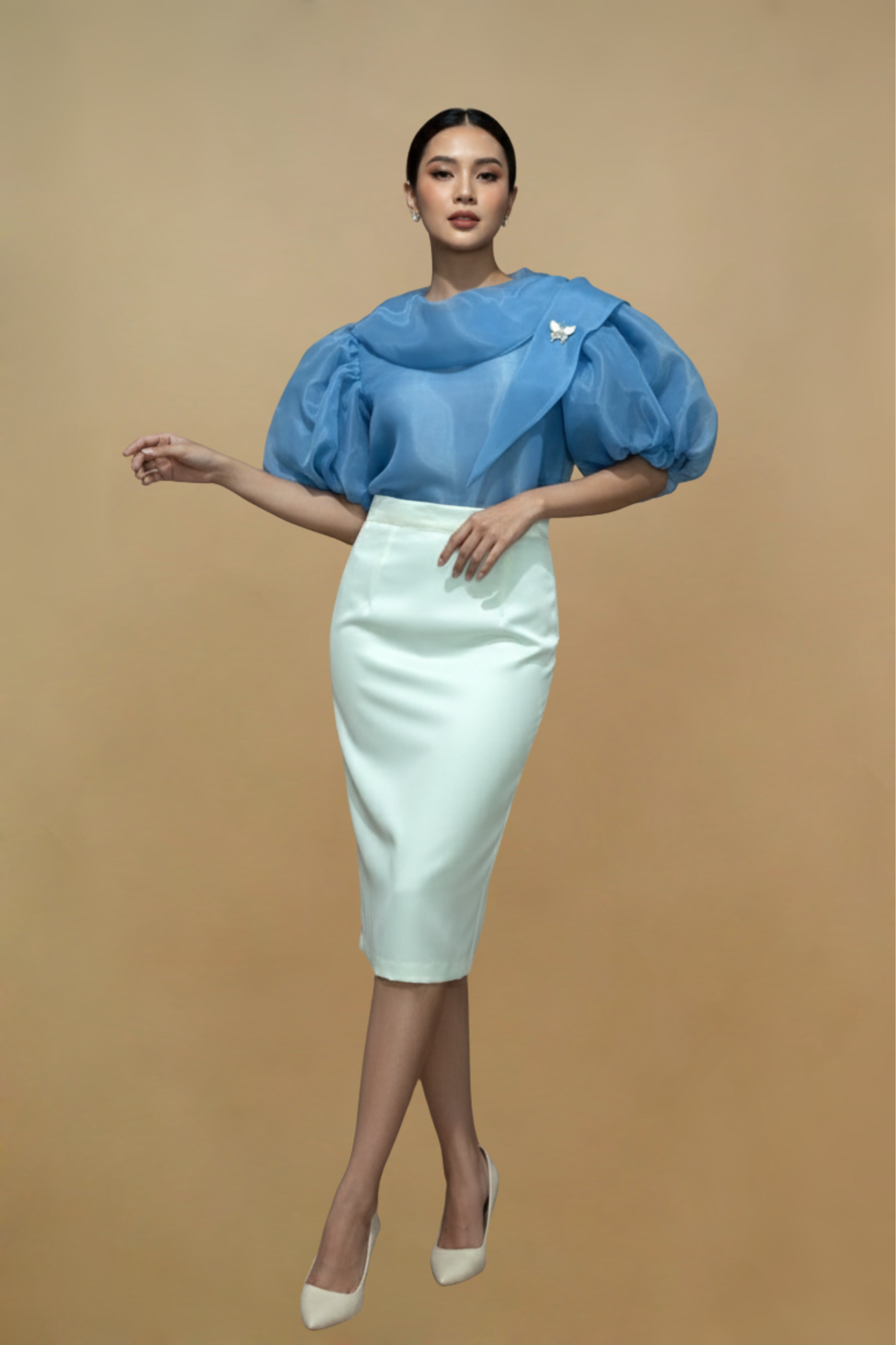 Woman wearing a blue Filipiniana kimona top and white skirt against a beige background